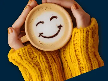 Highlight Accounting - Frothy mug of coffee with a smile detail in the foam held in a ladies hands with a yellow jumper pulled all the way to her palms