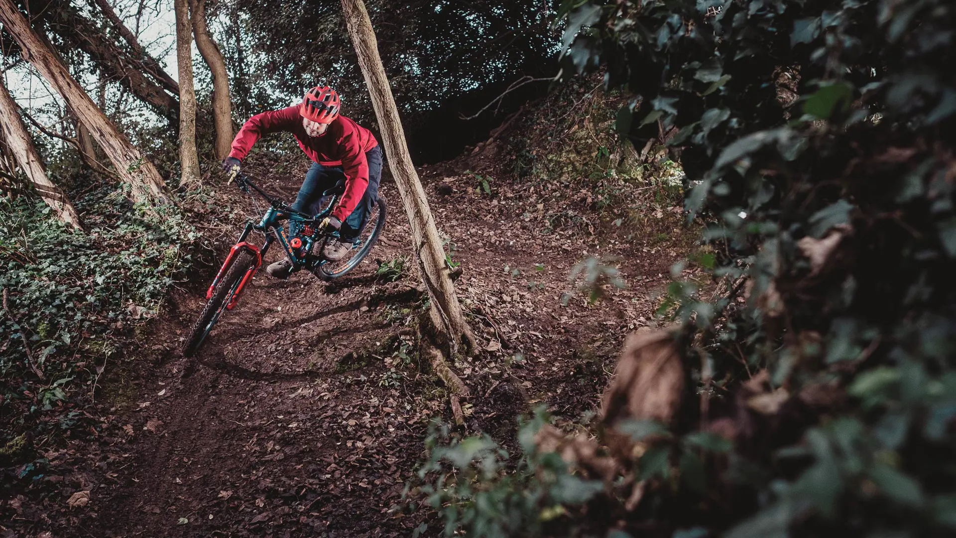 A photo of a young man riding his mountain bike round a sharp berm in woodland